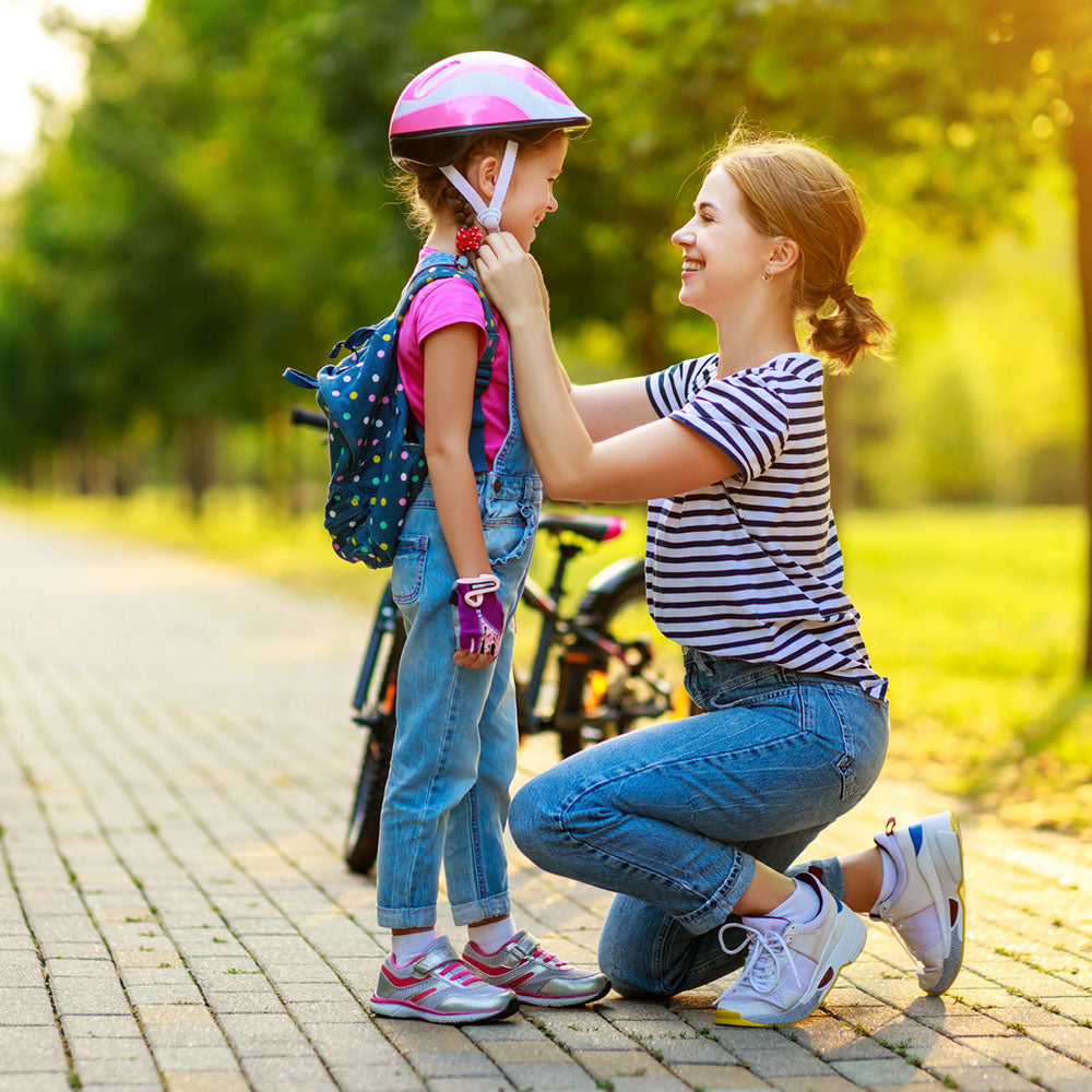 Mother helping her daughter with putting on her helmet before riding her bicycle.