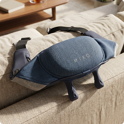 A blue and gray Miko massage pillow with four legs, resting on a beige fabric sofa in a warm, sunlit room.